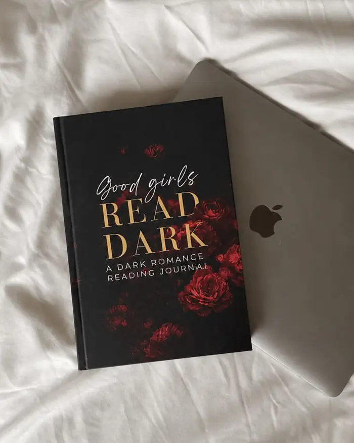 Good Girls Read Dark sobre una cama, junto a un portátil
